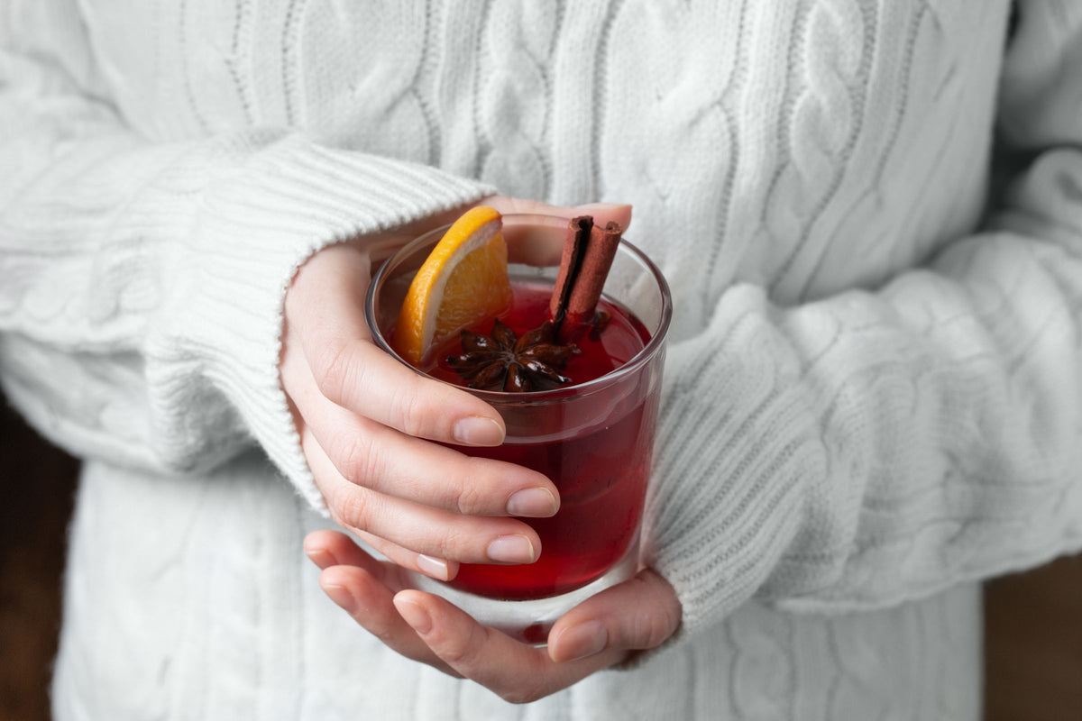 Händer i stickad tröja håller ett glas glögg med apelsin