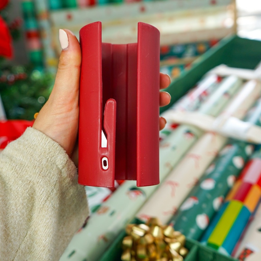En hand håller ett rött Julsnitt framför rullar med julpapper