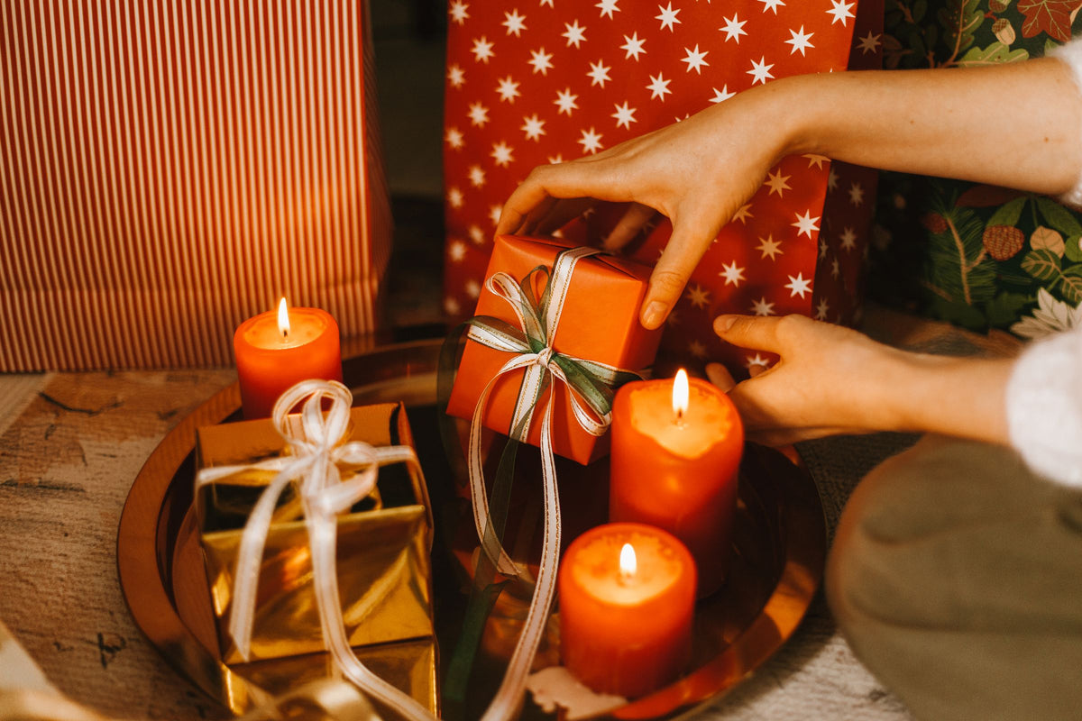 Händer som knyter ett snöre runt en julklapp bland tända ljus
